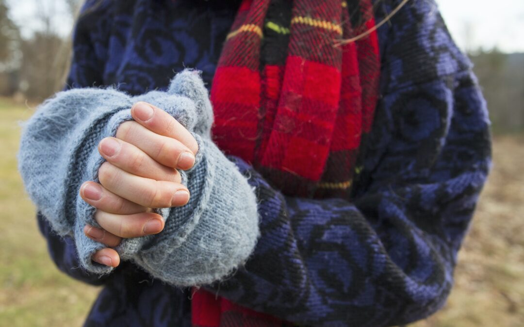 A woman in a tartan scarf and knitted woollen mitts, keeping her hands warm in cold weather.
